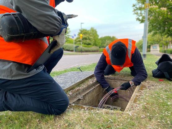 Two activists accessing cables under a manhole cover.