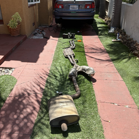 The complete exhaust removed from my 2003 BMW 530i donor car sits on my driveway, behind the blue 2003 BMW 530iT wagon, raised on QuickJack portable lifts, into which I'll be installing the exhaust.