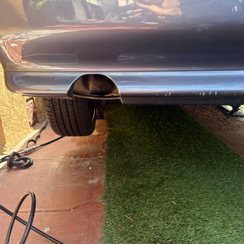 The exhaust cutout at the bottom of the rear bumper of my blue 2003 BMW 530iT wagon. The downturned exhaust tip, a feature of E39 sedans but not wagons, is deeply inset behind the cutout.
