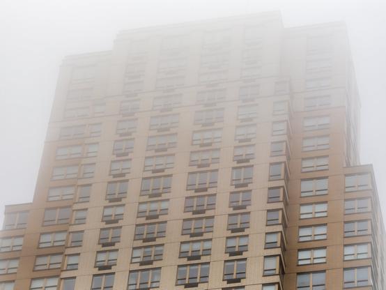 The top of a yellowish tall building disappears into a low-flying cloud.