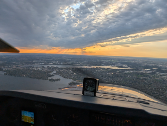 Looking out over the cowling on a plane towards an orange sunset with crepuscular rays.