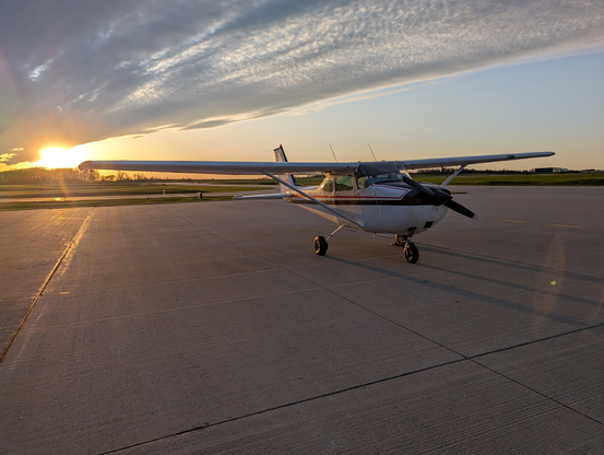 Aircraft parked at fuel pumps with the sun setting behind it making a nicely lit golden hour aircraft photo of a C172 Skyhawk