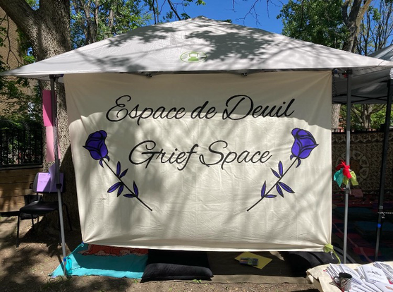 White banner stretched across the side of a pop-up tent; banner features paintings of two purple roses framing the words “grief space” painted in cursive in English and French