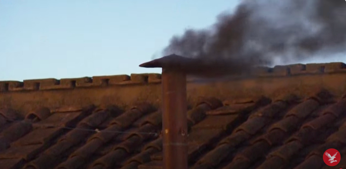 Schwarzer Rauch steigt aus einem Kamin. Dieser ragt aus einem Ziegeldach.Der Himmel ist silbern