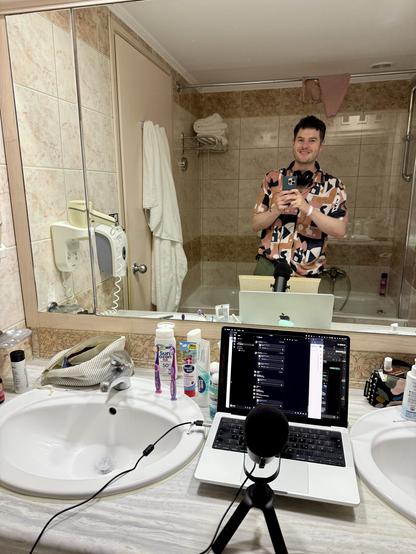 Spiegelselfie von Moritz, zwischen zwei Waschbecken steht ein Laptop und ein Mikrofon. Drum herum lauter Badutensilien
