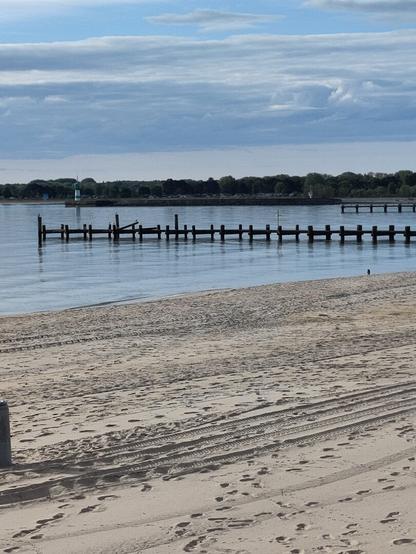 Sandstrand mit Holzsteg und Leuchtturm.