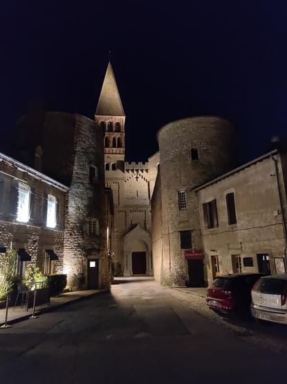 Vie nocturne sur l'église de Tournus éclairée par des spots, derrière une ancienne porte de la ville marquée par deux tours rondes.