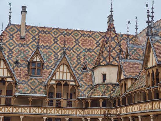 Vie sur le toit de l'hospice de Beaune avec des tuiles vernissées arrangés de manière géométrique avec des couleurs jaune, ocre, vert et noir. La toiture est surmontée de cheminées , fenêtre en chien assis, et autres petites toitures pointues.