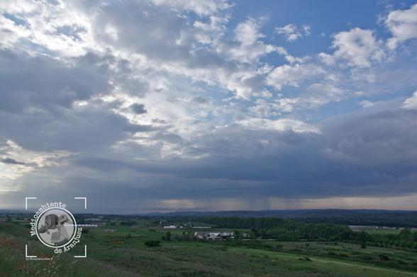 fotografía de la vega del río Tajo con las huertas de un verde intenso bajo un cielo nuboso y al fondo cortinas de lluvia