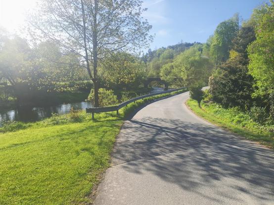 Geteert er Weg neben dem Fluß (Eder). Im Hintergrund eine wunderschöne Brücke mit Bögen.
Viel grün rundherum.