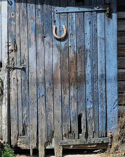 A distressed wooden door, which was once painted blue, and has a lucky horseshoe nailed to it.