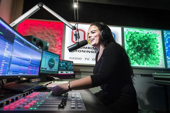 een enthousiaste jonge vrouw achter een microfoon in een radio studio