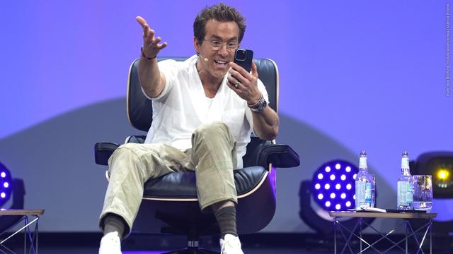 Ryan Reynolds, Schauspieler, Unternehmer und Mitbesitzer des walisischen Fußballclubs Wrexham AFC, telefoniert auf der Bühne mit seinen Kindern während der Digital- und Marketingmesse OMR in den Messehallen. (Foto: dpa Bildfunk, picture alliance/dpa | Marcus Brandt)