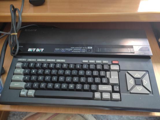 Un Sony hit bit hb75p, es un ordenador clásico.
Es un teclado de color negro con una gran parte trasera, tiene teclas negras y algunas teclas grises, el return, el control, los shift y algunas más. También hay un bloque de teclas de cursor, bien grandes, a la derecha