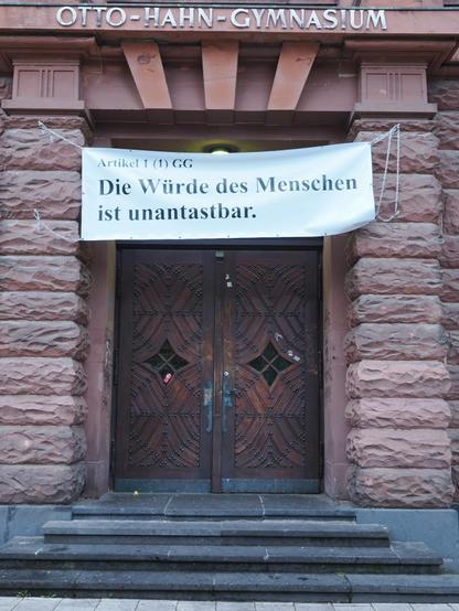 Eingang des Otto-Hahn-Gymnasiums in Saarbrücken. Über dem Eingang steht auf einem Banner: 
Artikel 1 (1) GG
Die Würde des Menschen ist unantastbar.