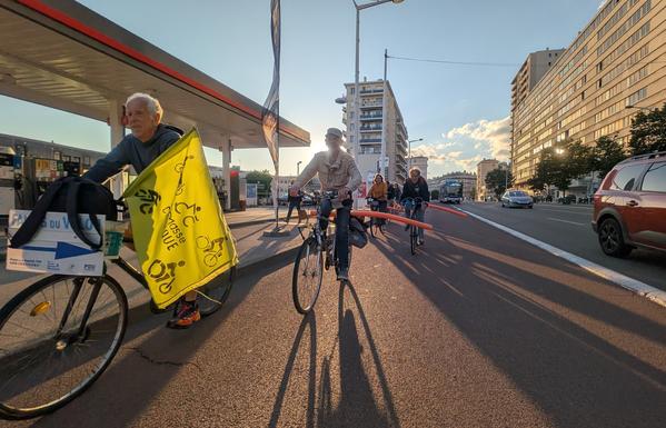 Photo d'une file de vélo sur une voie de bus. Le premier vélo a un drapeau Jaune de la Masse Critique, et les vélos derrière lui on une frite de piscine pour matérialiser la distance de sécurité.