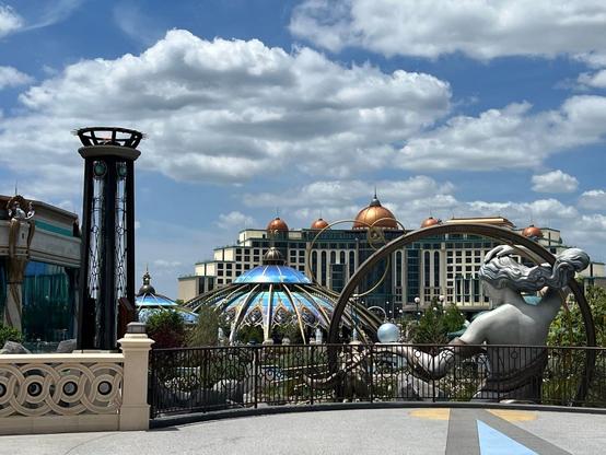 A large building with bronze domes stands out on the horizon with a statue of Luna, the goddess of the moon, in the foreground in Epic Universe, Orlando, Florida.