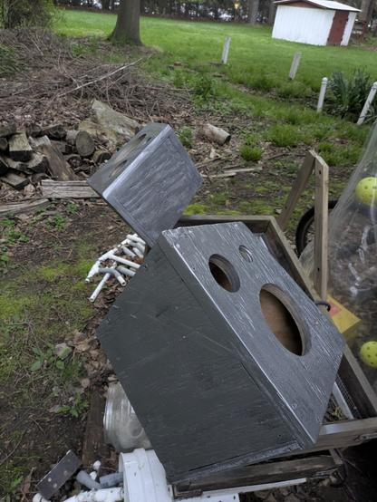 The two silver speaker enclosures (see photo 4 alt-text), with no speakers, are hanging in the air for the silver paint to dry. My neighbor's green yard with a little white shed is visible.