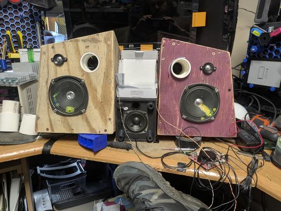 Early mockup of the boombox (see photo 4 alt-text): speakers without any paint (except some half-assed red paint on the right speaker box), ugly drivers set in them (with several repair patches on the cones), and an exposed 2.5 inch subwoofer between them. Some guy's shoe is in the frame, as are various wires and work clutter.