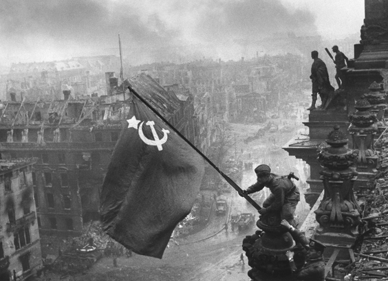 Red army soldier waving soviet flag over destroyed Reichstag
