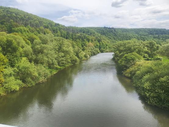 Blick auf einen breiten Fluss (Eder) links sind Hügel mit grünen Bäumen, rechts Wald und Wiesen.