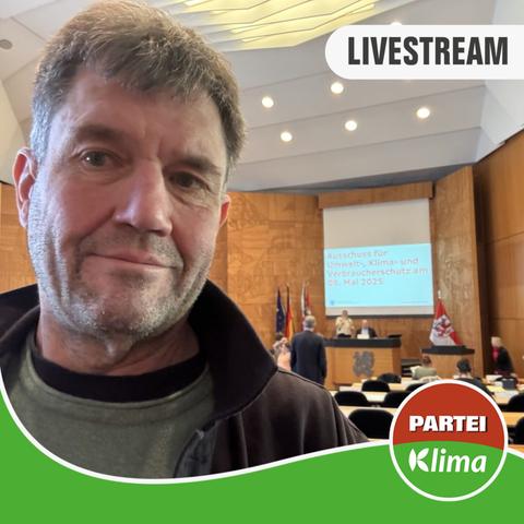 Selfie mit Christopher Schrage auf der linken Seite mit Blick auf den Plenarsaal und die Leinwand hinter dem Podium während einer Sitzung des Ausschusses für Klima-, Umwelt-und Verbraucherschutz