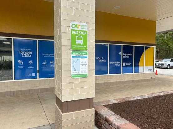 the two bus stop signs at the tanger outlet tilton, with the one above a standard green, yellow, and white cat (concord area transit) sign, and the one below containing a map of the laconia route and the times the bus stops at the mall