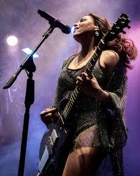 Cantora Pitty ao microfone com sua guitarra em uma performance ao vivo.