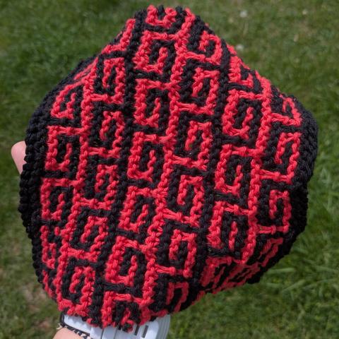 Red knit washcloth with black Greek Key motif. Grass in background.