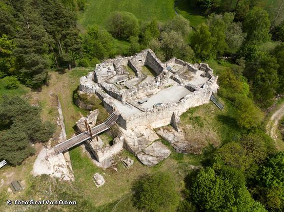 Restaurierte Grundmauern einer Höhenburg auf einem Granitfelsen mit einer modernen Holzbrücke als Zugang