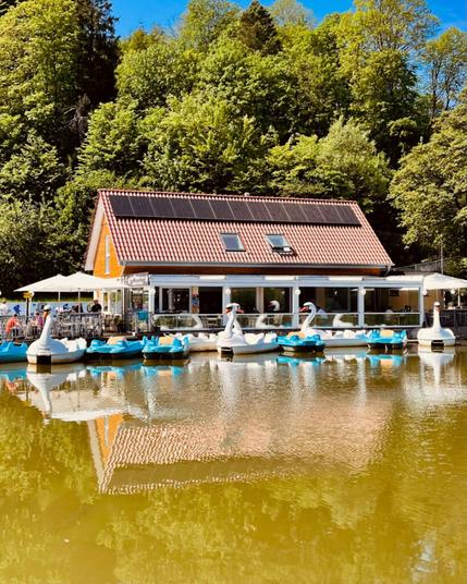 Tretboote auf einem See direkt vor einem Café. Einige Tretboote sehen aus wie Schwäne.
