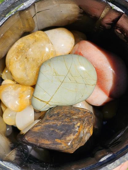 tumbled stones from beachcombing. green and red but mostly yellow quartz with one red and one dark slate gray with orange highlights