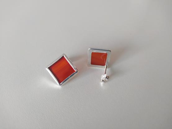 a pair of silver earrings with square red gemstone.