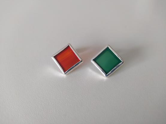 two silver earrings with square gemstones. The left has a red gemstone and the right has a green one