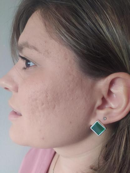 a woman is wearing a square green and silver earring