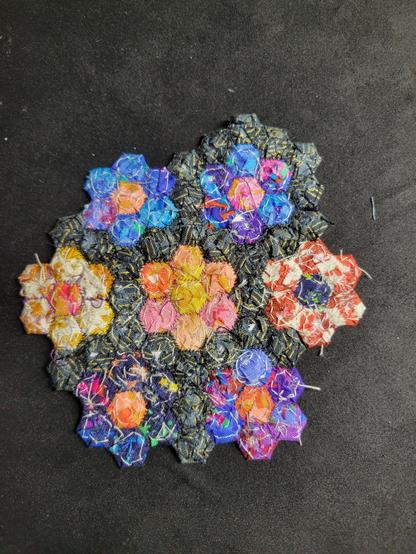 Photograph of the back, which has a really interesting rough and fuzzy texture. The shapes are less well defined and the colours sometimes bleed into one another. The white and black tacking threads are visible and the paper templates can just about be glimpsed.