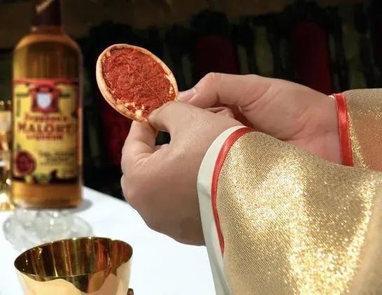 Pope hands holding a tiny Chicago deep dish pizza like it was a communion wafer. Bottle of Malört in the background instead of wine