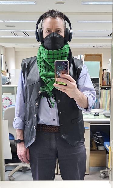 a photo of me in the staff room mirror wearing: headphones, fauxhawk, green & black keffiyeh, faux leather vest, blue & white striped shirt, between belt, and greyish pants