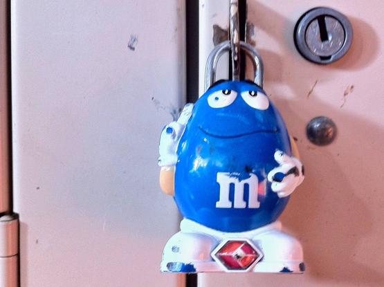 It was a Tuesday. It’s always a Tuesday. I lit a mental cigarette and looked at the scene—locker 214, guarded by a beat-up blue M&M with the expression of someone who knew too much and cared too little. He wasn’t just a lock, he was a warning. Chipped paint, eyes full of hard candy disillusionment. I’d seen types like him before—colorful on the outside, hollow in the middle. The kind of plastic that doesn’t break, just slowly fades. What was he guarding? Dirty sneakers? Evidence? A sandwich from 2008? Didn’t matter. He wasn’t talking. Just hung there, looking smug, like the world was the punchline to a bad joke written by a marketing exec on a deadline. But I’d crack the case. I always do. I’m just not sure I’ll like what I find behind that door.