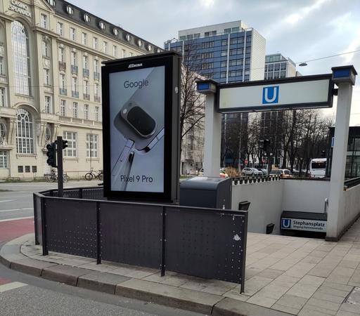 Massiver Bildschirm mit Google-Konsumpropaganda prangt am Straßenrand vor einer U-Bahn-Station (Stephansplatz)