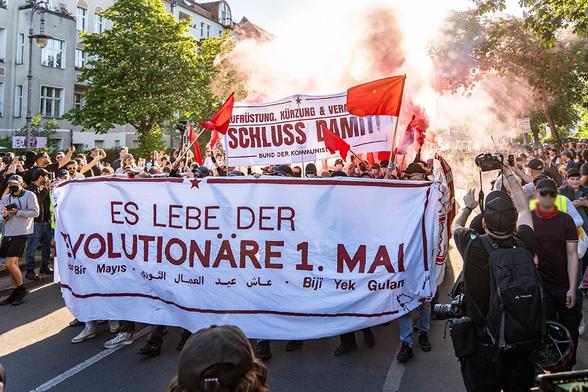 Das Foto zeigt demonstrierende Menschen hinter dem Fronttransparent mit dem Text Es lebe der revolutionäre 1. Mai in verschiedenen Sprachen