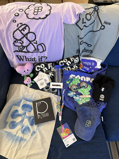 Top-down view of Chi's Figma Config 2025 haul displayed on a couch. Two large Figma-themed T-shirts with illustrated designs are draped at the back. The haul includes plushies, multiple smaller shirts, a water bottle, various stickers and pins, a black cap, a denim cap with a green Figma logo, and a black book titled 'Practice.' Chi's event badge with attached pins and a lanyard is centered in the display, laid over an airsprayed bandana featuring the Figma logo.
