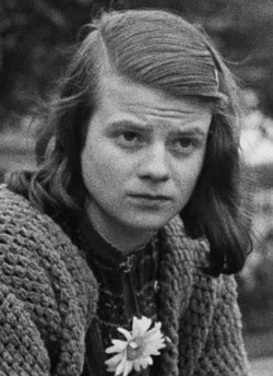 photo, greyscale, Sophie Scholl in 1942, young woman, shoulderlong brown hair, looking left, thoughtful serious expression, wearing woolen jacket, daisy stuck on the front of her jacket