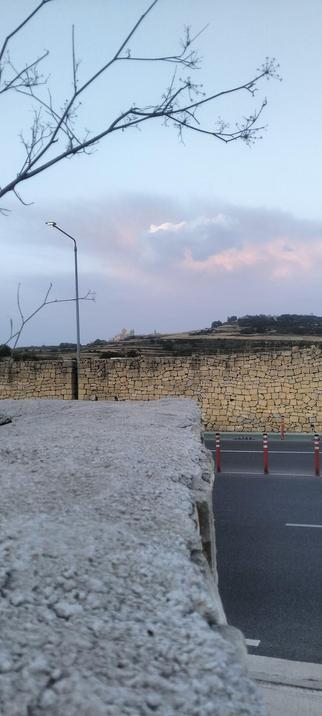 Another shot of Mdina rising up in the distance of the Pre dawn sky, in the foreground a 10 foot tall - dry limestone wall separates the countryside from the.road that runs alongside it.