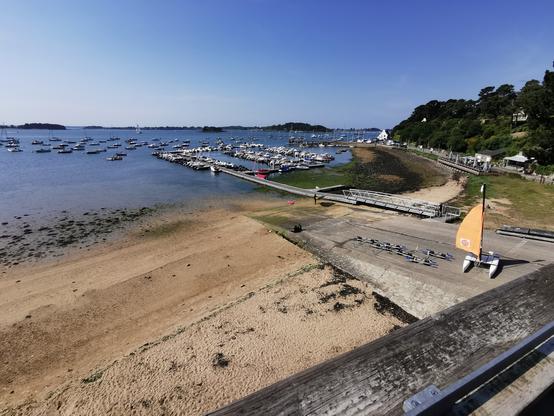 Une vue d'un port avec une plage au premier plan. La mer en arrière-plan avec des îles au loin.