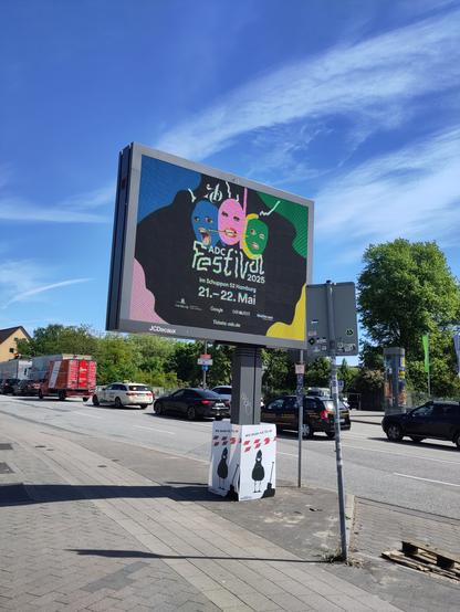 Helles Riesendisplay, das über den Weg ragt. Um die Stelze sind vier A0-"Bauplakate" gruppiert.