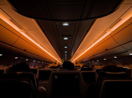 Low light shot of dark interior aircraft cabin, silhouetted seat backs with light bars on the roof leading toward towards the front.