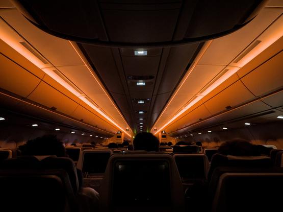 Low light shot of dark interior aircraft cabin, silhouetted seat backs with light bars on the roof leading toward towards the front.
