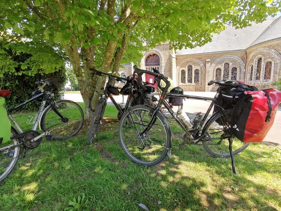 4 vélos à l'ombre sous un arbre devant une église.