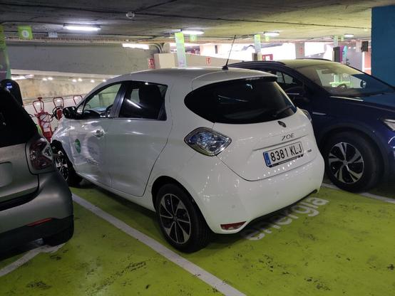 Un Ecotxe vist per darrera aparcat sobre una plaça d'aparcament per a vehicles elèctrics de la Plaça dels Patins de Palma. El flanquegen altres cotxes a banda i banda.